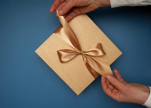 paper gift box with ribbon on isolated blue background unpacking by human hands