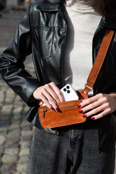 woman posing outside in jeans, white sweater and leather jacket with a small orange belt bag