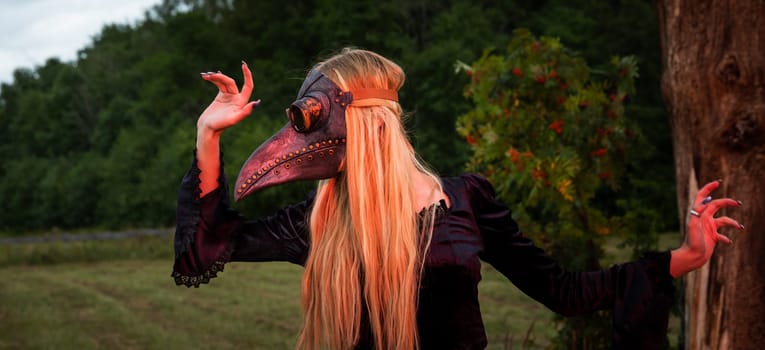 Natures beauty with a touch of mystery. A mystical and captivating image - a blonde woman in a crow mask posing near a withered tree in nature, creating an aura of mystery and beauty.