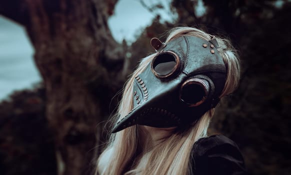 Natures beauty with a touch of mystery. A mystical and captivating image - a blonde woman in a crow mask posing near a withered tree in nature, creating an aura of mystery and beauty.