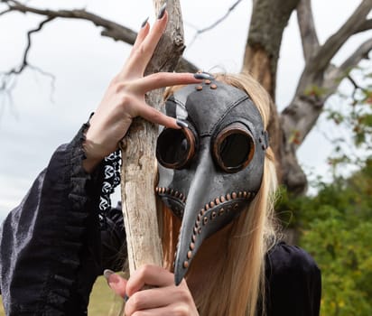 Natures beauty with a touch of mystery. A mystical and captivating image - a blonde woman in a crow mask posing near a withered tree in nature, creating an aura of mystery and beauty.