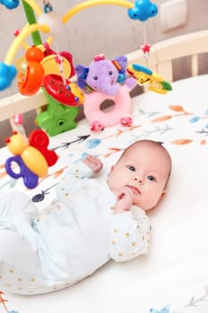smiling cute newborn baby playing with mobile in crib at home