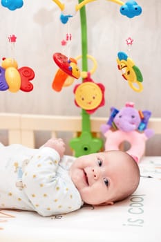 smiling cute newborn baby playing with mobile in crib at home