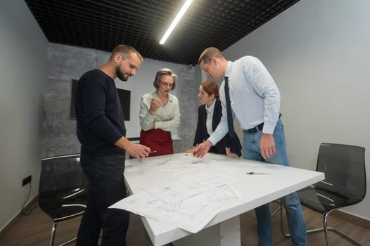 Four business people review and discuss blueprints. Designers engineers at a meeting