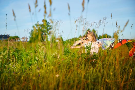 Pretty blonde girl and small boy with bright butterfly wings having fun in meadow or field on natural landscape with grass and flower on sunny summer or spring day. Brother and sister together