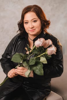 a stylish adult woman in black leather clothes stands with a bouquet of pink roses in the interior.
