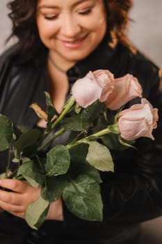 a stylish adult woman in black leather clothes stands with a bouquet of pink roses in the interior.