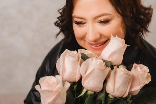 a stylish adult woman in black leather clothes stands with a bouquet of pink roses in the interior.