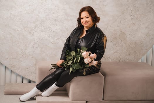 a stylish adult woman in black leather clothes is sitting with a bouquet of pink roses in the interior.