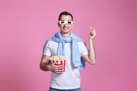 handsome man in 3d glasses, white t-shirt showing popcorn on pink background
