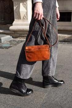 young brunette posing outside in jeans, white sweater with a small orange handbag