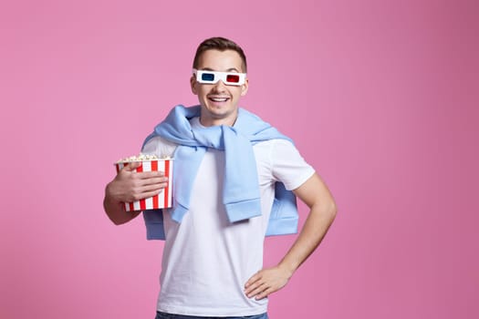 handsome man in 3d glasses holding bucket of popcorn on pink background