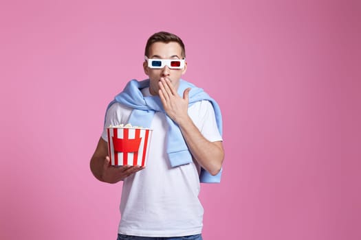 scared handsome man in 3d glasses holding bucket of popcorn on pink background