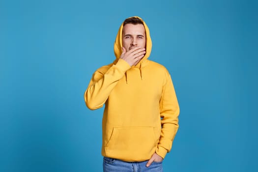 yawning man in yellow sweatshirt isolated on blue background.