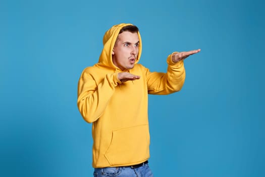positive funny man in yellow sweatshirt dancing on blue background