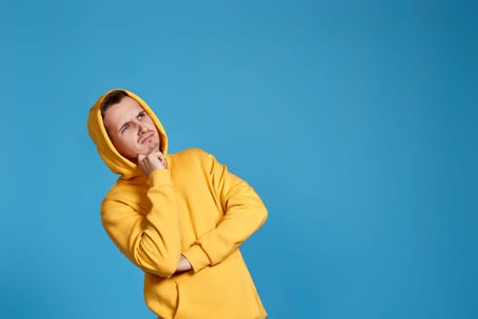 handsome thoughtful man holding arms folded, touching chin with hand and looking at the side on blue background. copy space