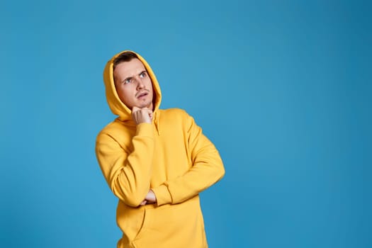 handsome thoughtful man holding arms folded, touching chin with hand and looking at the side on blue background. copy space