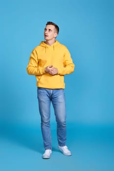 thoughtful young man thinking and looking at the side on blue background. Full length