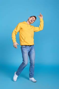 cheerful young handsome man dancing on blue background. Full body
