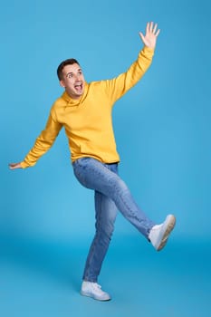 happy funny young man in yellow sweatshirt and jeans isolated on blue background.