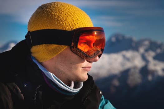 Male skier overlooking snow covered mountains on a sunny day, sun beams reflection in ski goggles.