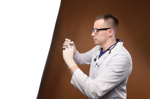Portrait of young male doctor drawing Covid-19 vaccine from vaccine bottle, with syringe and stethoscope, Covid-19 vaccination concept.