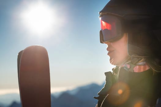 Close-up, ski goggles and a woman's face in a ski resort against the backdrop of mountains and sky on a sunny day.