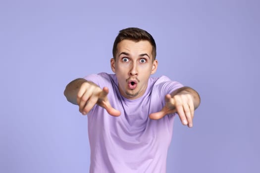 amazed caucasian man pointing finger at you on pastel violet background