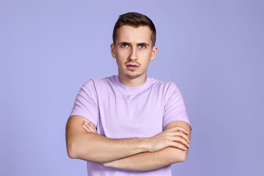 calm young guy posing with crossed arms and looking at the camera on pastel purple studio background