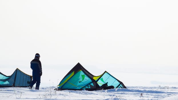 A man stands with his back to green tents in a snowy winter terrain.