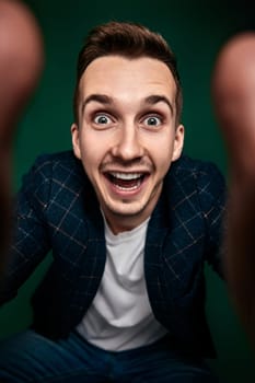 close-up portrait of young man in plaid jacket looking at camera with hands on green background.
