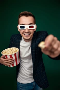 young man in 3d glasses showing popcorn on green background.
