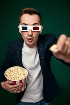 young man in 3d glasses showing popcorn on green background.