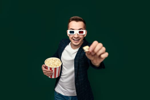 young man in 3d glasses showing popcorn on green background.