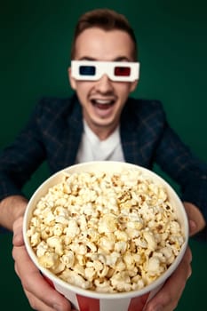 very excited handsome man holding big bucket of popcorns on green background. focus on popcorn