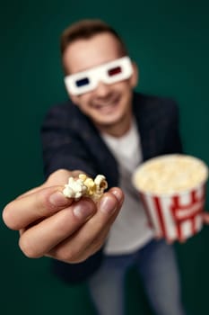 young man in 3d glasses showing popcorn on green background. focus on hand