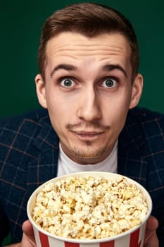 close-up portrait of handsome man holding big bucket of popcorns on green background