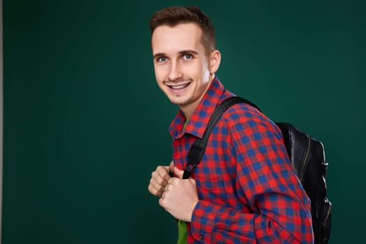 cheerful handsome man in red plaid shirt with backpack looking at camera on green background. copy space