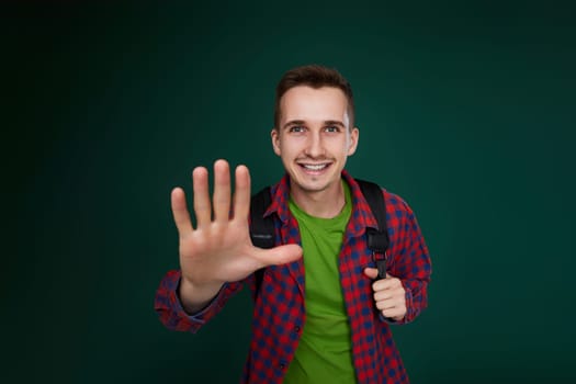 cheerful handsome man in red plaid shirt with backpack looking at camera on green background. guy says hi