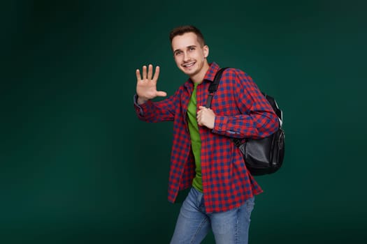cheerful handsome man in red plaid shirt with backpack looking at camera on green background. copy space
