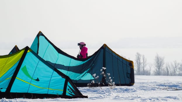 A girl in a pink jumpsuit stands behind tents in snowy winter terrain.