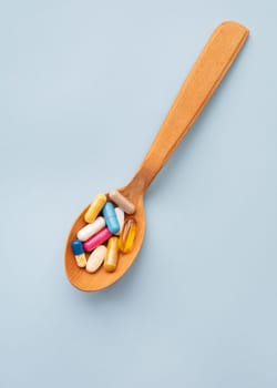 Various bright pills on a blue background lie in a wooden spoon. The concept of healthcare and evidence-based medicine, close-up