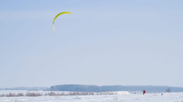 man in red pulling a yellow kite in the field,man snowkiting in the field. man in black pulling a green kite in the field,man snowkiting in the field. Kitesurfer ride the parachute in the wind among the snow.