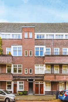 Amsterdam, Netherlands - 10 April, 2021: an apartment building with cars parked on the street in front of it and blue sky overhead over the top floor