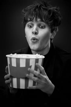 portrait of crazy young man holding bucket of popcorn and grimacing . black and white