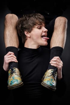young sexy handsome guy hugs male legs in bright shoes on black background. fashion