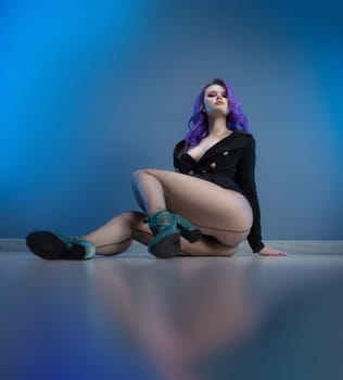 sexy girl in a fashionable jacket and with purple hair poses erotically in her underwear on a blue background of a copy paste