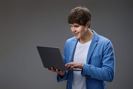 Cheerful caucasian man using laptop computer for online communication, typing messages isolated on gray background