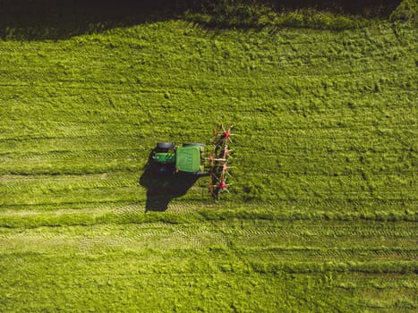 Aerial view of a tractor mowing a green fresh grass field, a farmer in a modern tractor mowing a green fresh grass field on a sunny day. High quality photo