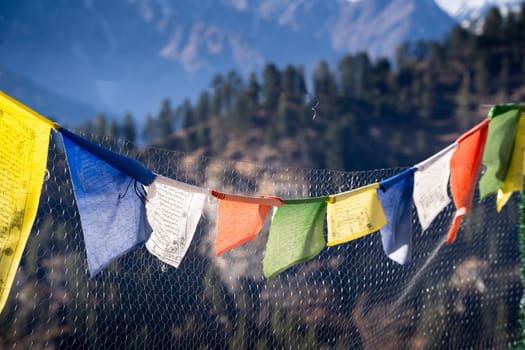 sacred religious multicolored prayer flags on fence moving in the wind showing a bhuddist prayer incantation common in hill stations in Himachal Pradesh India